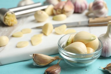 Photo of Fresh peeled garlic cloves in bowl on light blue wooden table, closeup. Organic product