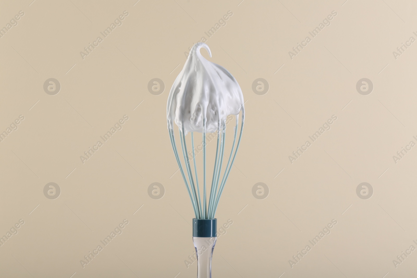 Photo of Whisk with whipped cream on beige background