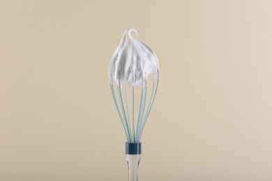 Whisk with whipped cream on beige background