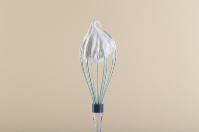 Photo of Whisk with whipped cream on beige background