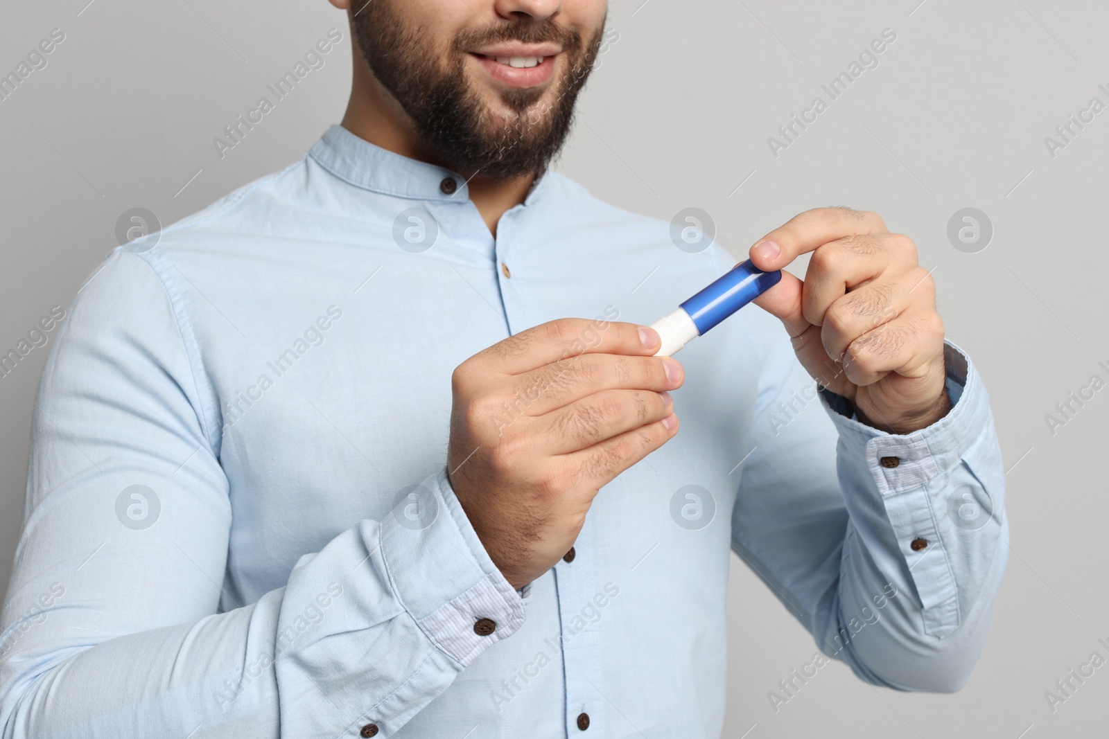 Photo of Young man with lip balm on grey background, closeup