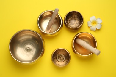 Photo of Golden singing bowls, mallets and flower on yellow background, flat lay