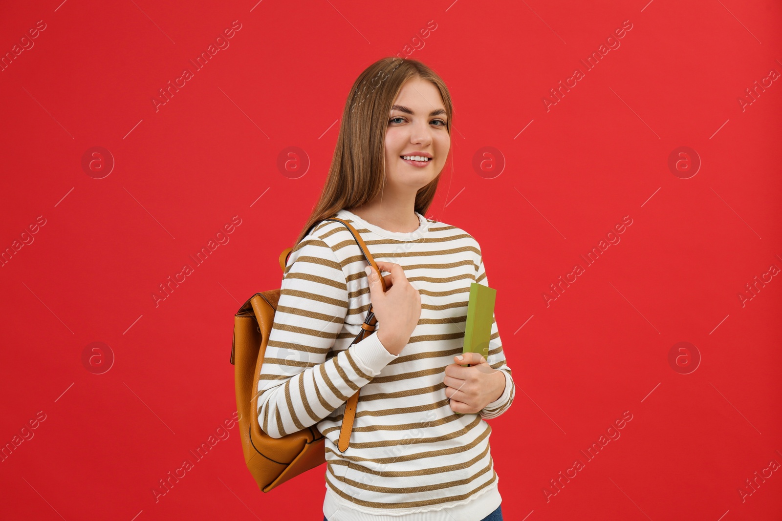 Photo of Teenage student with backpack and book on red background