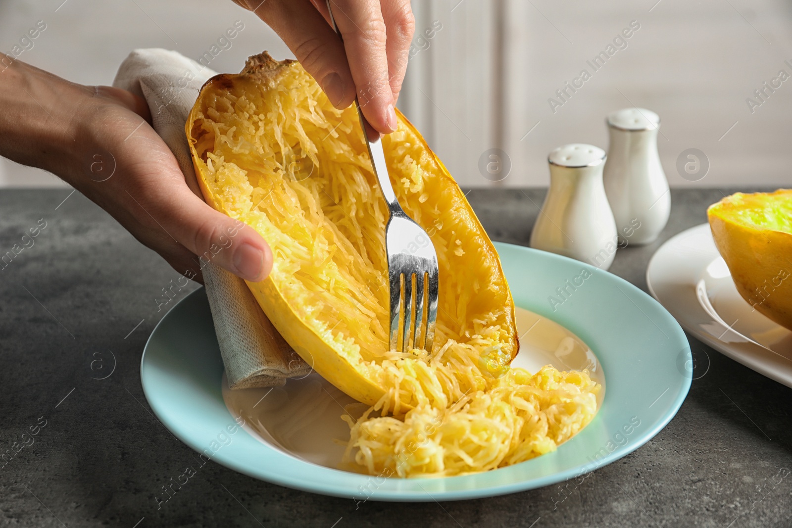 Photo of Woman scraping flesh of cooked spaghetti squash with fork on table, closeup