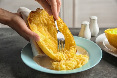 Woman scraping flesh of cooked spaghetti squash with fork on table, closeup