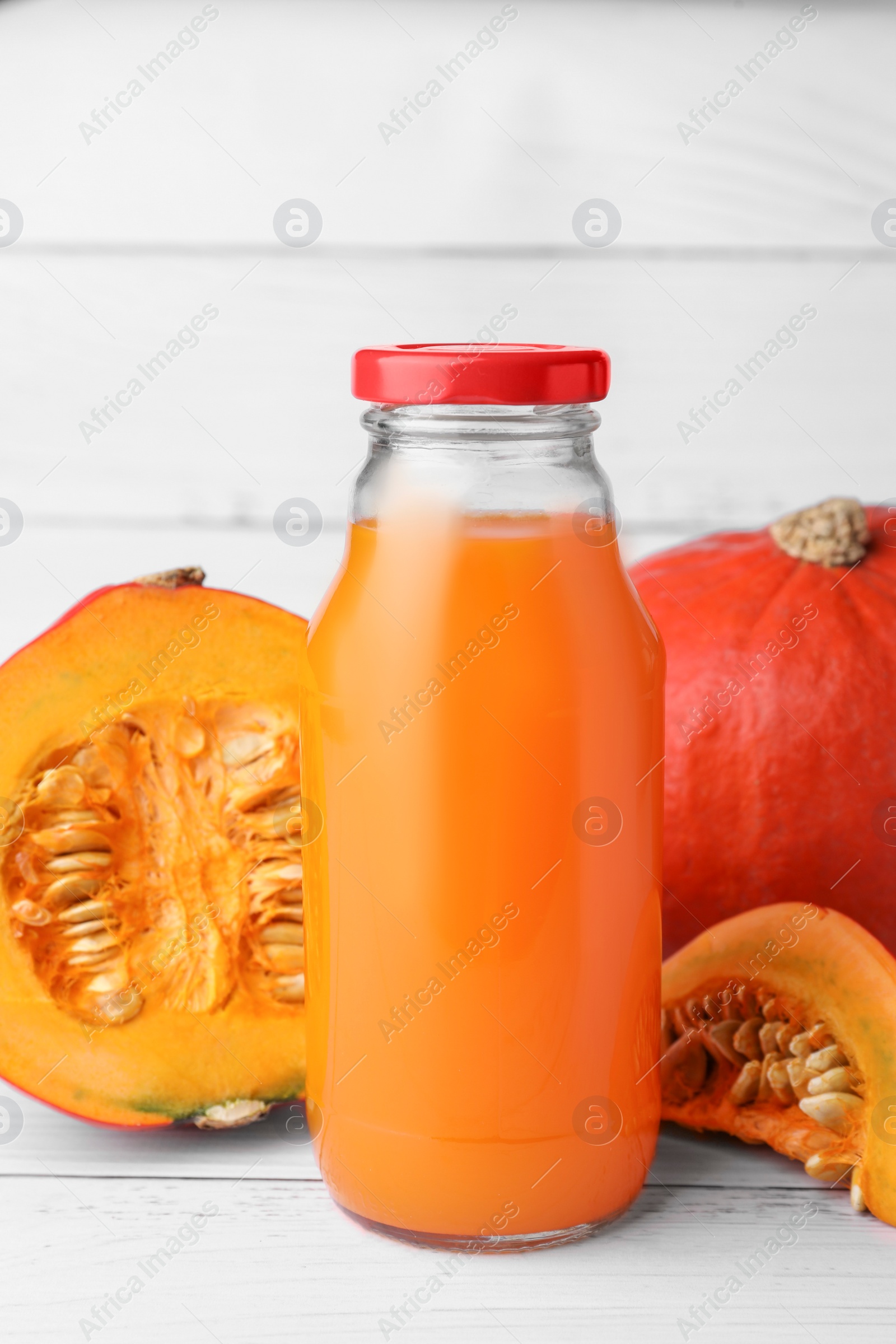 Photo of Tasty pumpkin juice in glass bottle, whole and cut pumpkins on white wooden table