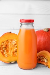 Photo of Tasty pumpkin juice in glass bottle, whole and cut pumpkins on white wooden table
