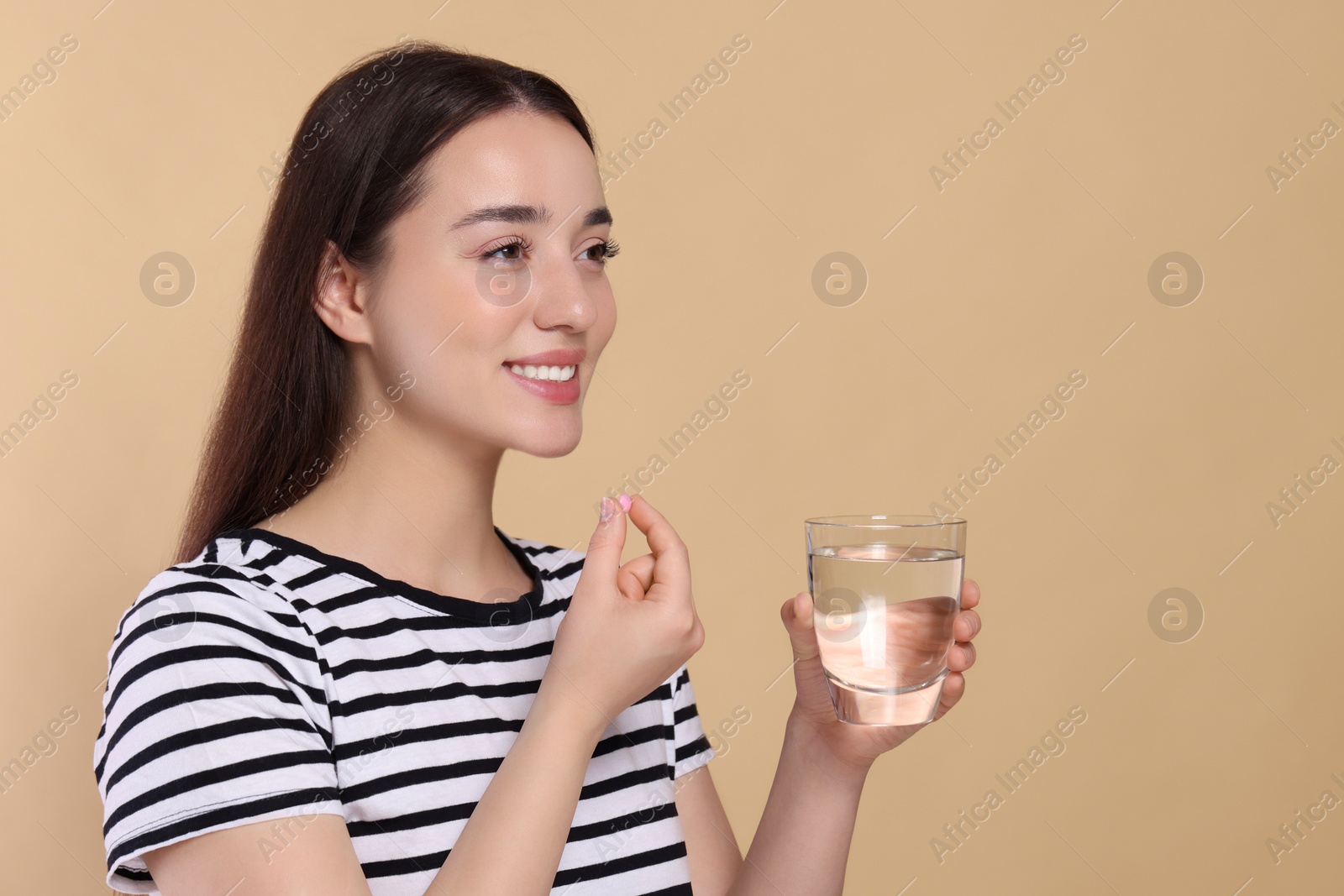 Photo of Happy woman with glass of water taking pill on beige background, space for text