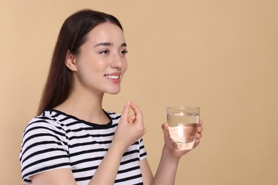 Photo of Happy woman with glass of water taking pill on beige background, space for text