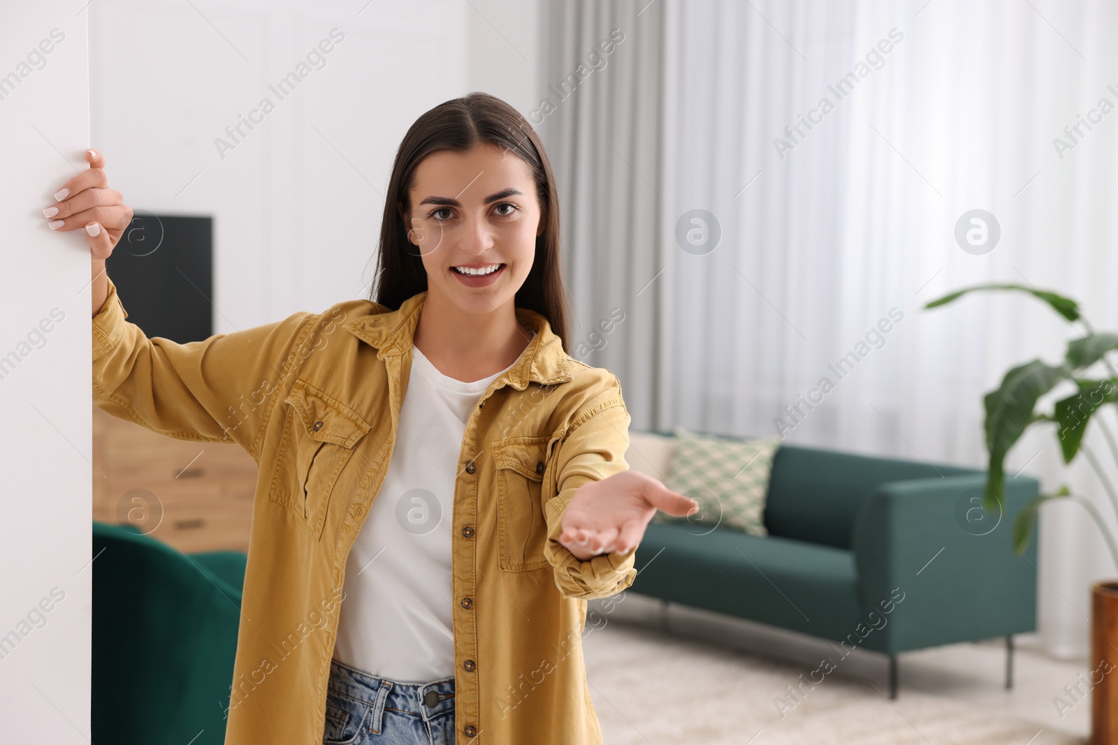Photo of Happy woman welcoming near white wall at home, space for text. Invitation to come in room