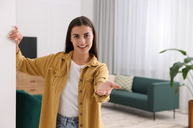 Photo of Happy woman welcoming near white wall at home, space for text. Invitation to come in room