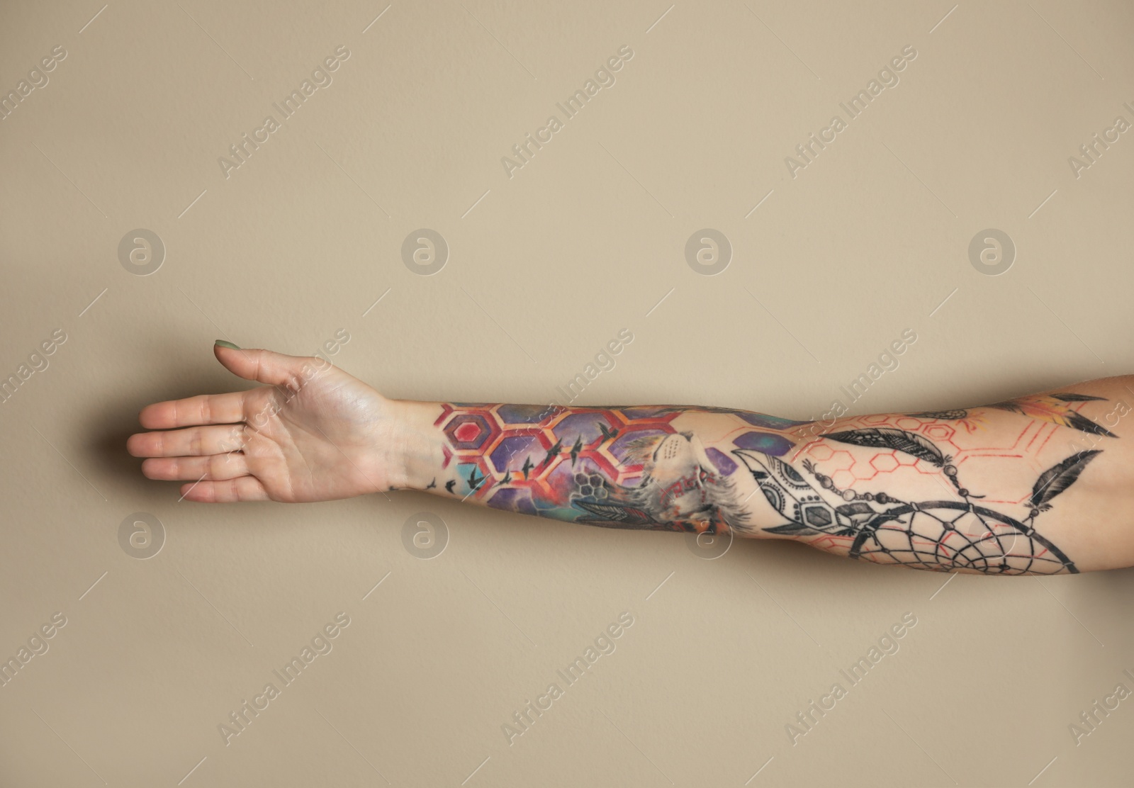 Photo of Woman with colorful tattoos on arm against beige background, closeup