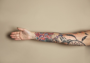 Photo of Woman with colorful tattoos on arm against beige background, closeup