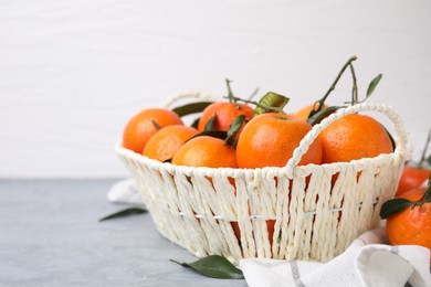 Photo of Basket with fresh ripe tangerines and leaves on grey table, space for text