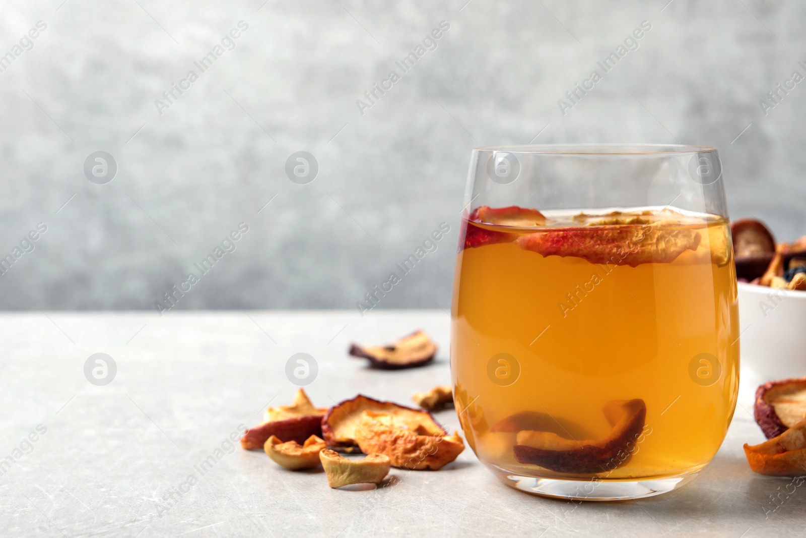 Photo of Delicious compote with dried apple slices in glass on grey table, space for text