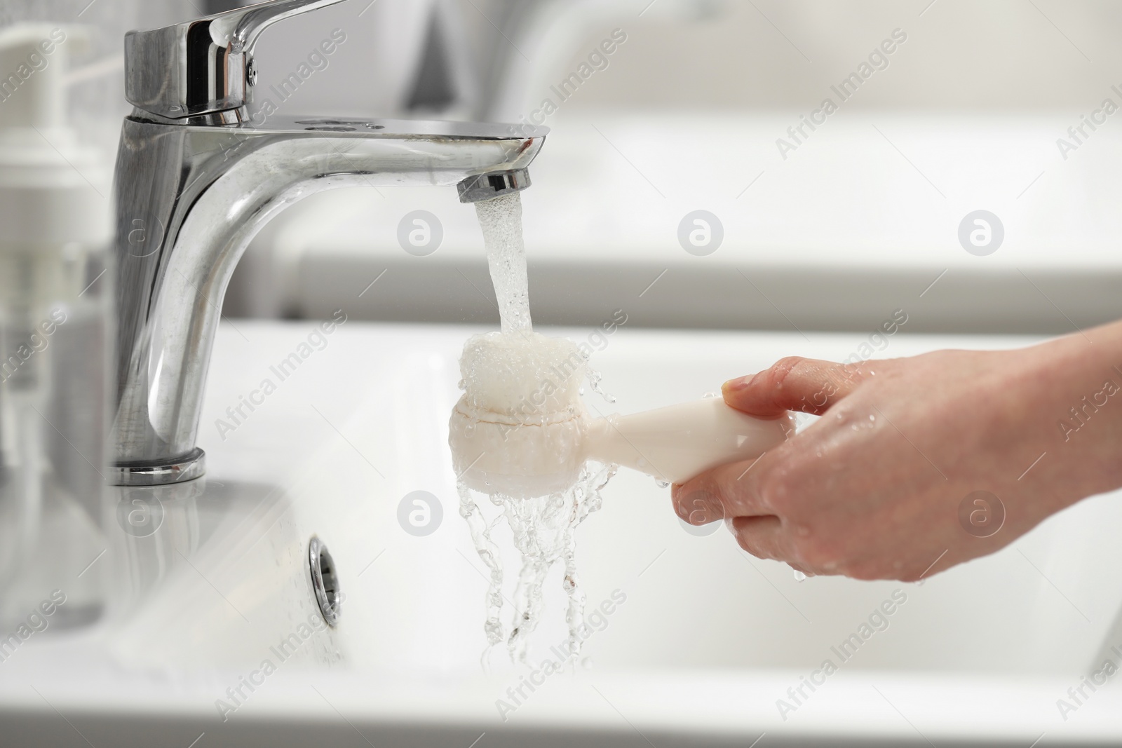 Photo of Young woman washing facial brush in bathroom, closeup