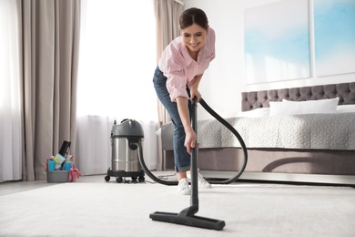 Photo of Woman removing dirt from carpet with vacuum cleaner at home