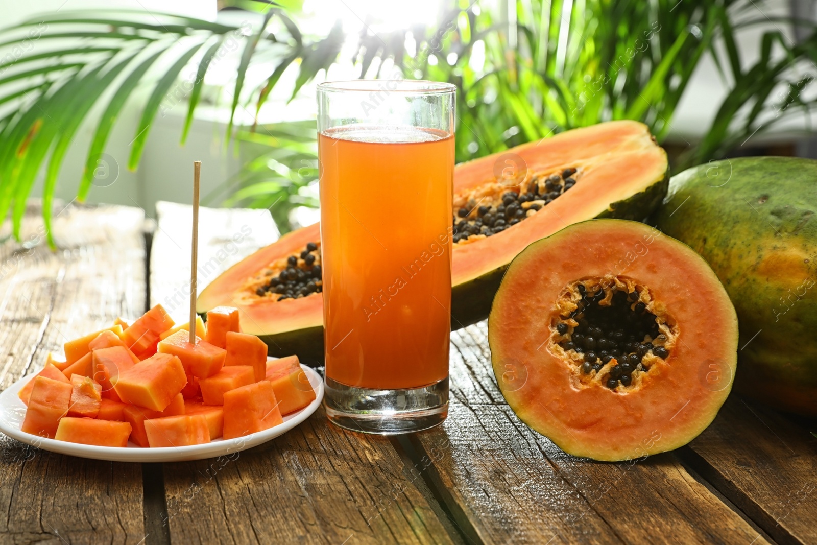 Photo of Fresh papayas and juice on wooden table against blurred background