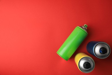Cans of different graffiti spray paints on red background, flat lay. Space for text