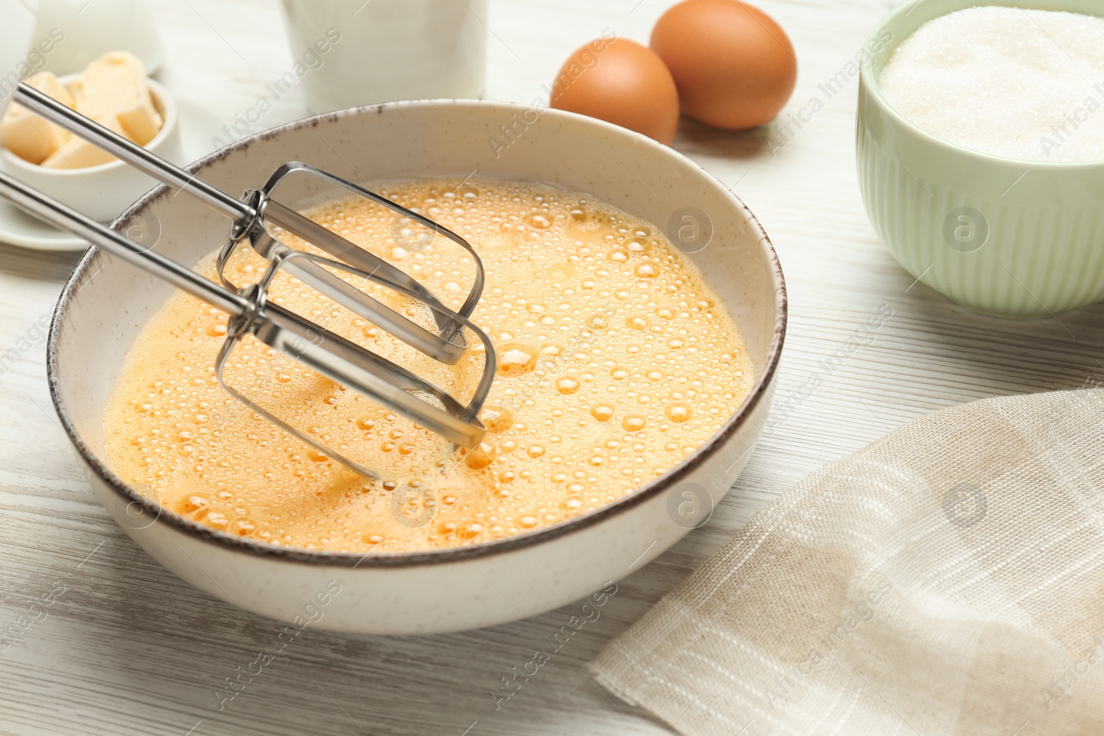 Photo of Beating eggs in bowl with mixer at white wooden table, closeup