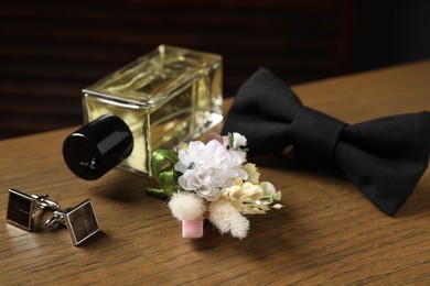 Photo of Wedding stuff. Stylish boutonniere, perfume bottle, bow tie and cufflinks on wooden table, closeup