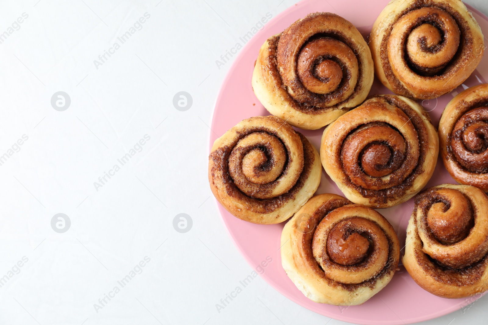Photo of Many tasty cinnamon rolls on white table, top view. Space for text