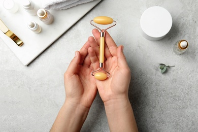 Photo of Woman with natural face roller at grey table, top view
