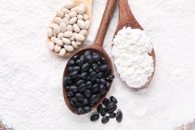 Wooden spoons with different seeds on kidney bean flour, flat lay