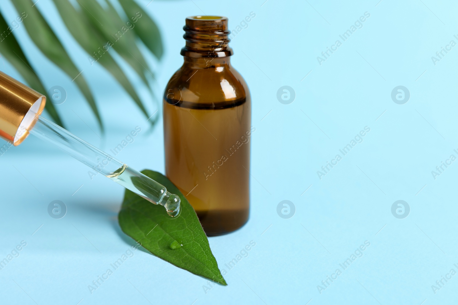 Photo of Dripping cosmetic oil from pipette into leaf on light blue background, closeup. Space for text