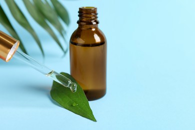 Dripping cosmetic oil from pipette into leaf on light blue background, closeup. Space for text