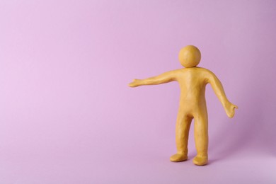 Photo of Human figure with arms wide open made of yellow plasticine on violet background. Space for text