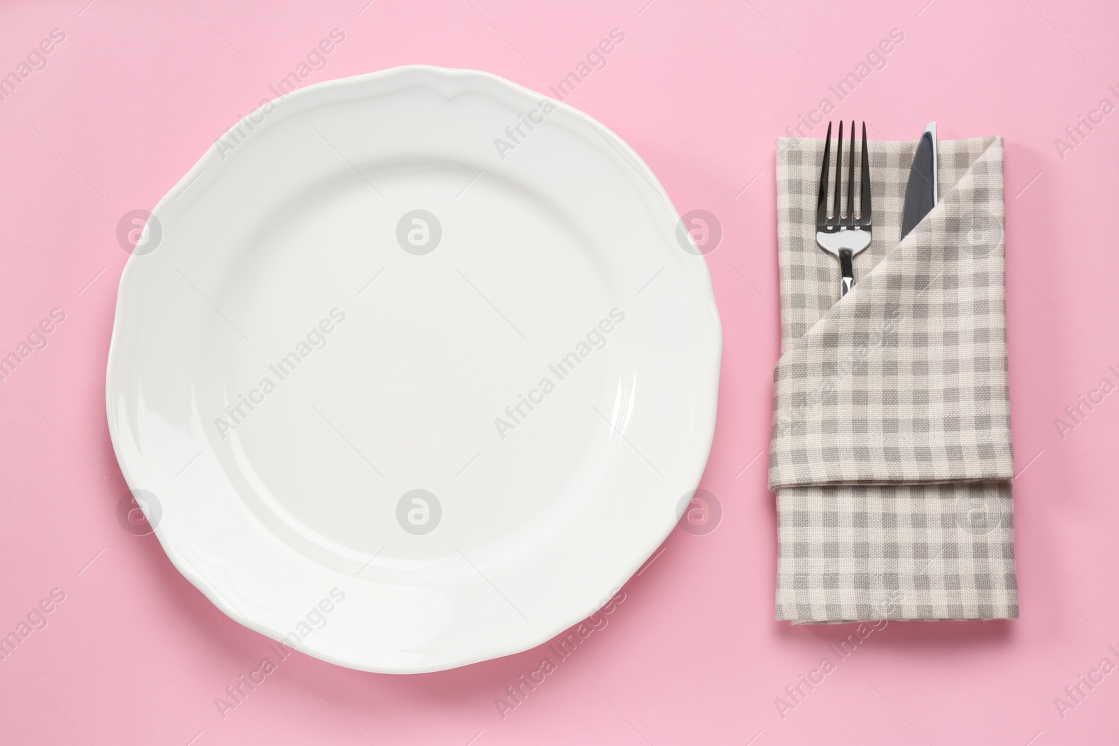Photo of Clean plate and cutlery wrapped in napkin on pink background, flat lay