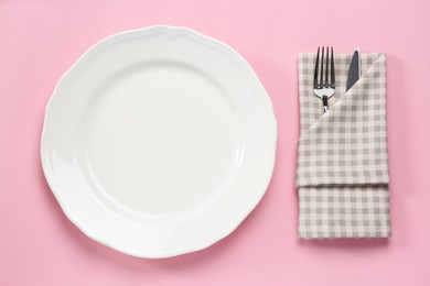 Clean plate and cutlery wrapped in napkin on pink background, flat lay