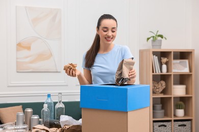 Garbage sorting. Smiling woman throwing crumpled paper into cardboard box in room