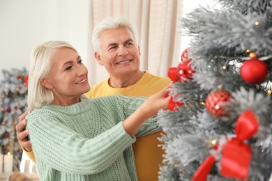 Happy mature couple decorating Christmas tree at home