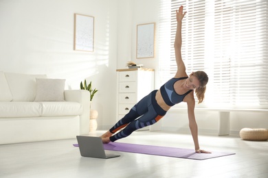 Photo of Woman having online video class via laptop at home. Distance yoga course during coronavirus pandemic