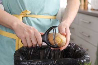 Woman peeling fresh potato above garbage bin indoors, closeup