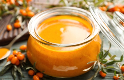 Delicious sea buckthorn jam and fresh berries on blue wooden table, closeup