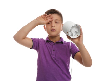 Little boy with portable fan suffering from heat on white background. Summer season