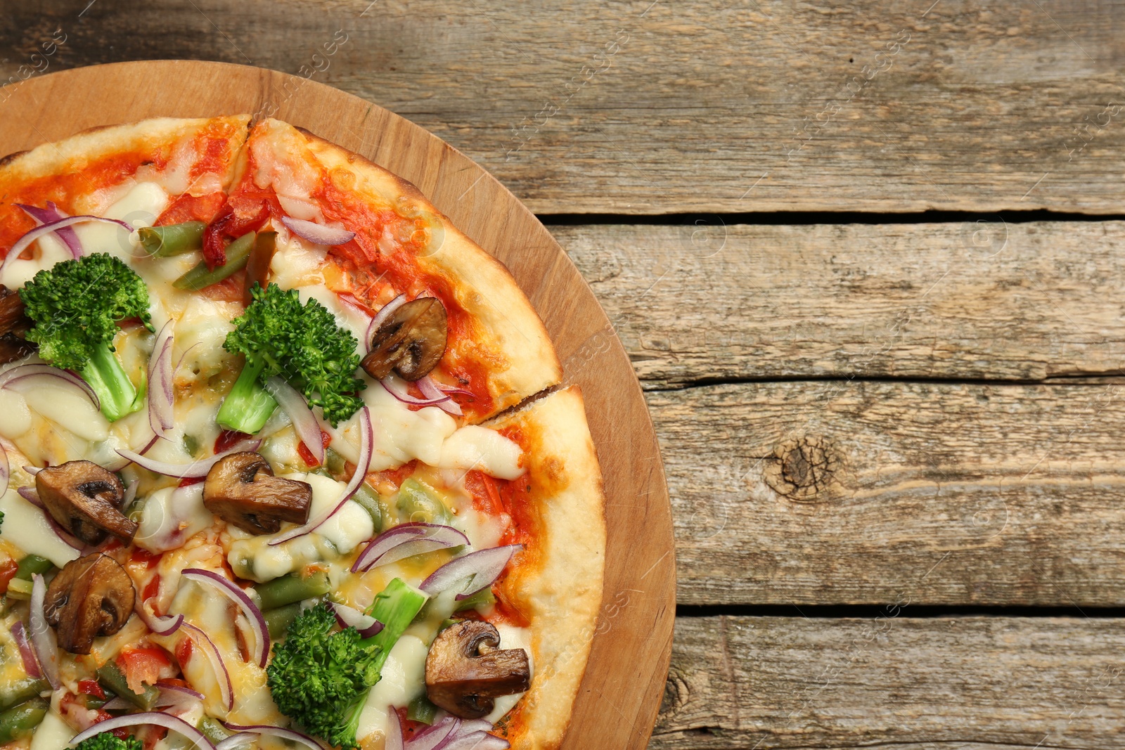 Photo of Board with delicious vegetarian pizza on wooden table, top view. Space for text