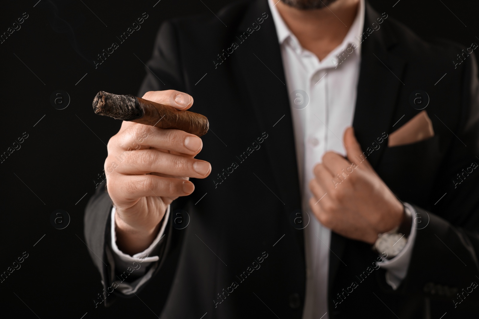 Photo of Man in elegant suit smoking cigar on black background, closeup