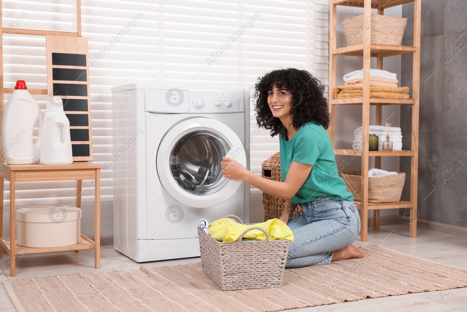 Photo of Happy woman with laundry near washing machine indoors