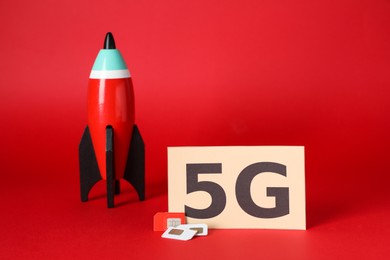 Internet concept. Paper with phrase 5G, toy rocket and SIM cards on red background