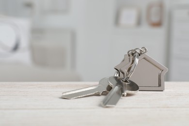Photo of Keys with keychain in shape of house on wooden table against blurred background, closeup. Space for text