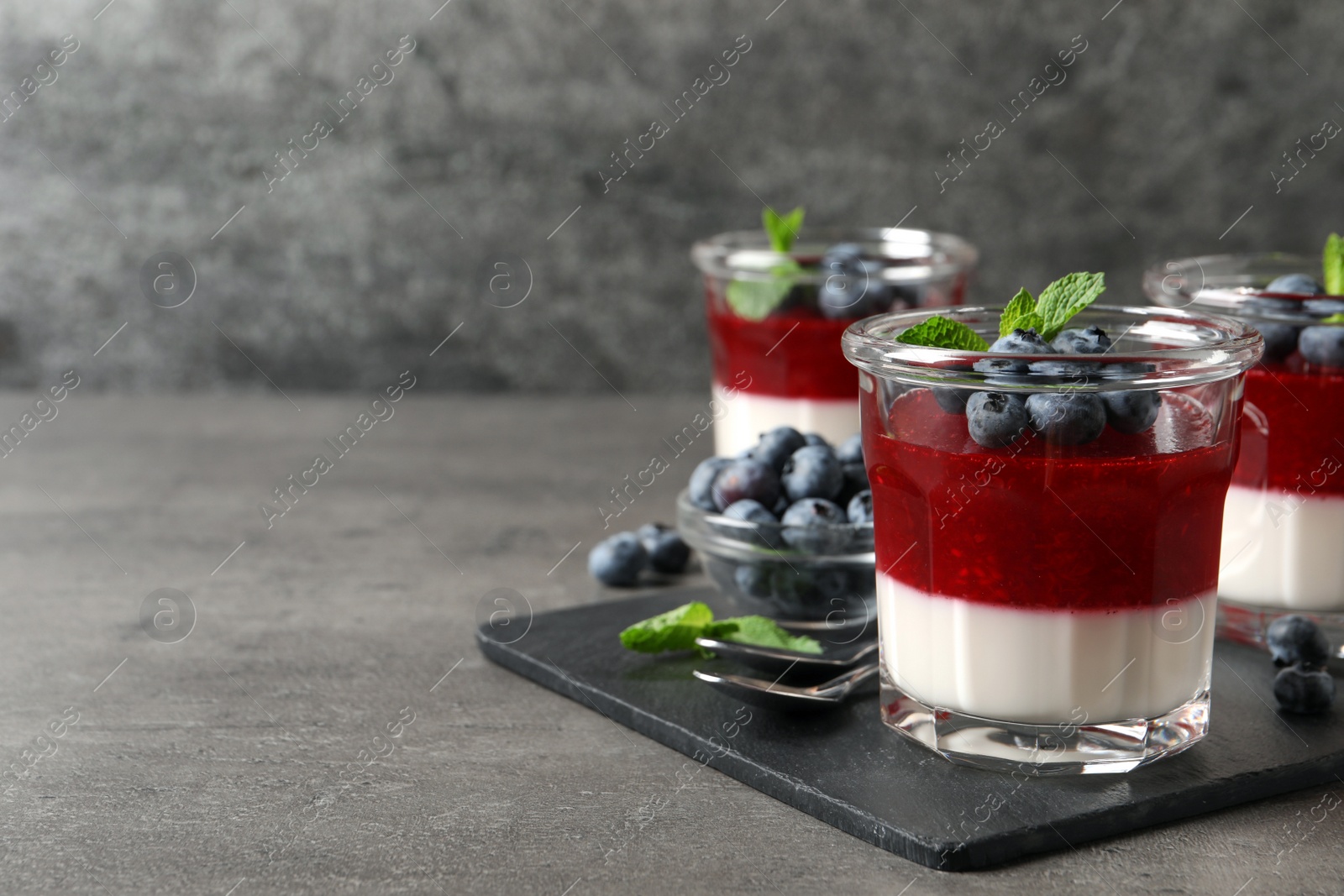 Photo of Delicious panna cotta with fruit coulis and fresh blueberries served on grey table. Space for text