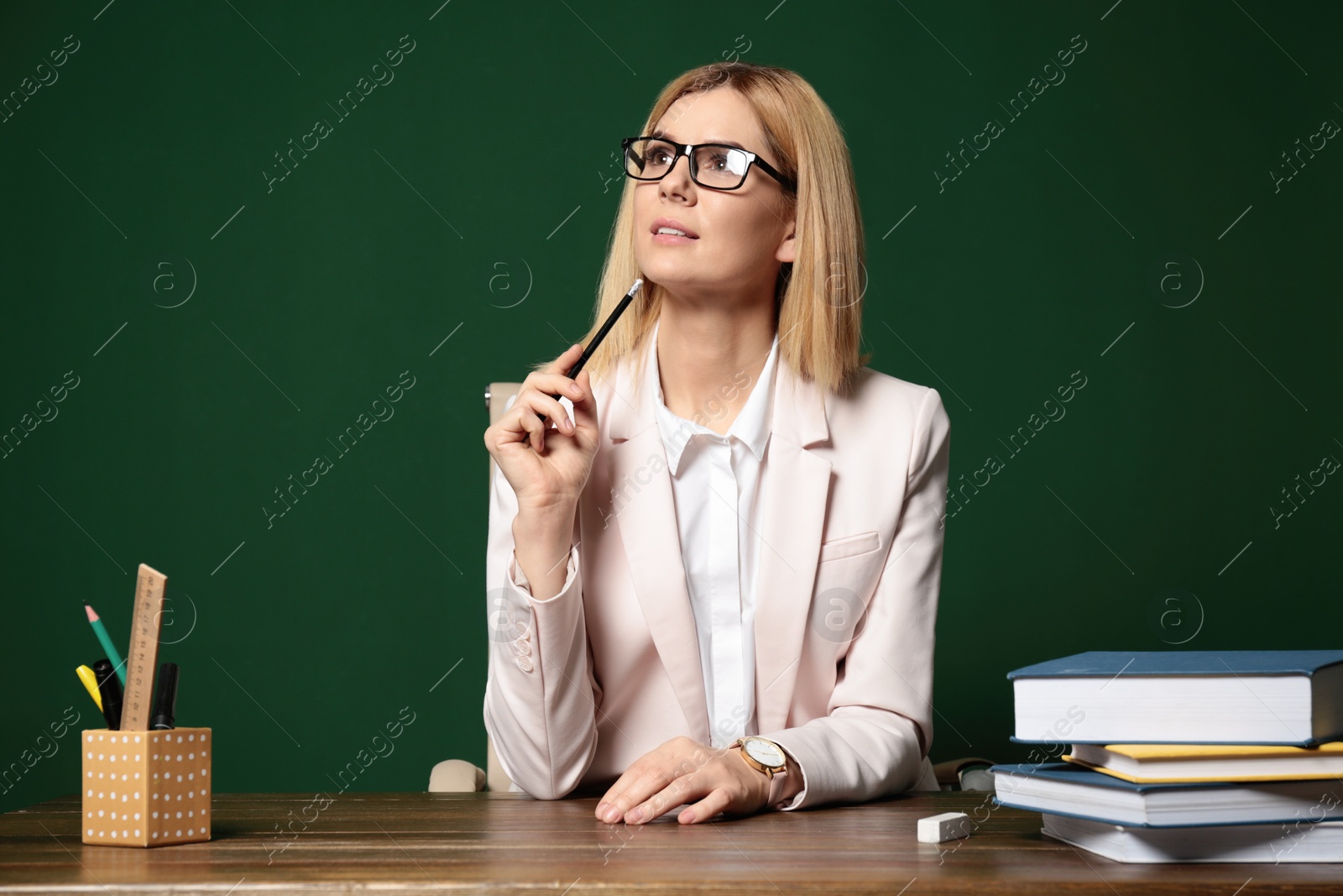 Photo of Portrait of beautiful teacher sitting at table near chalkboard