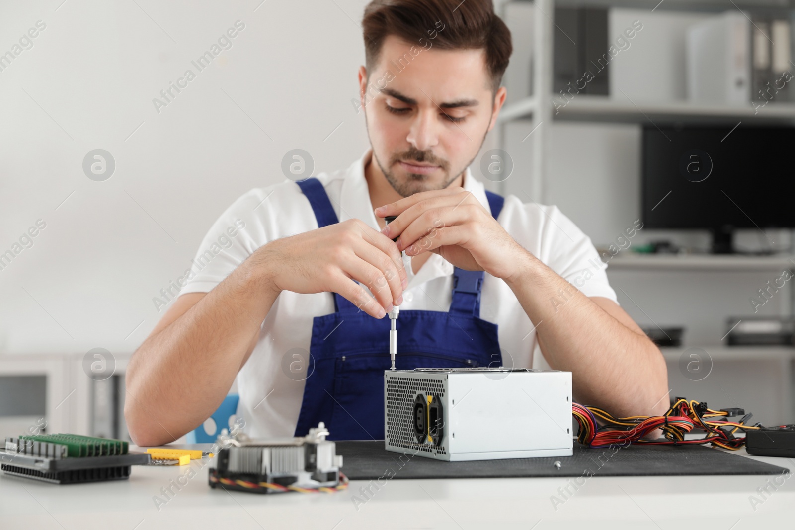 Photo of Male technician repairing power supply unit at table indoors