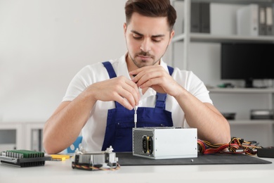 Male technician repairing power supply unit at table indoors