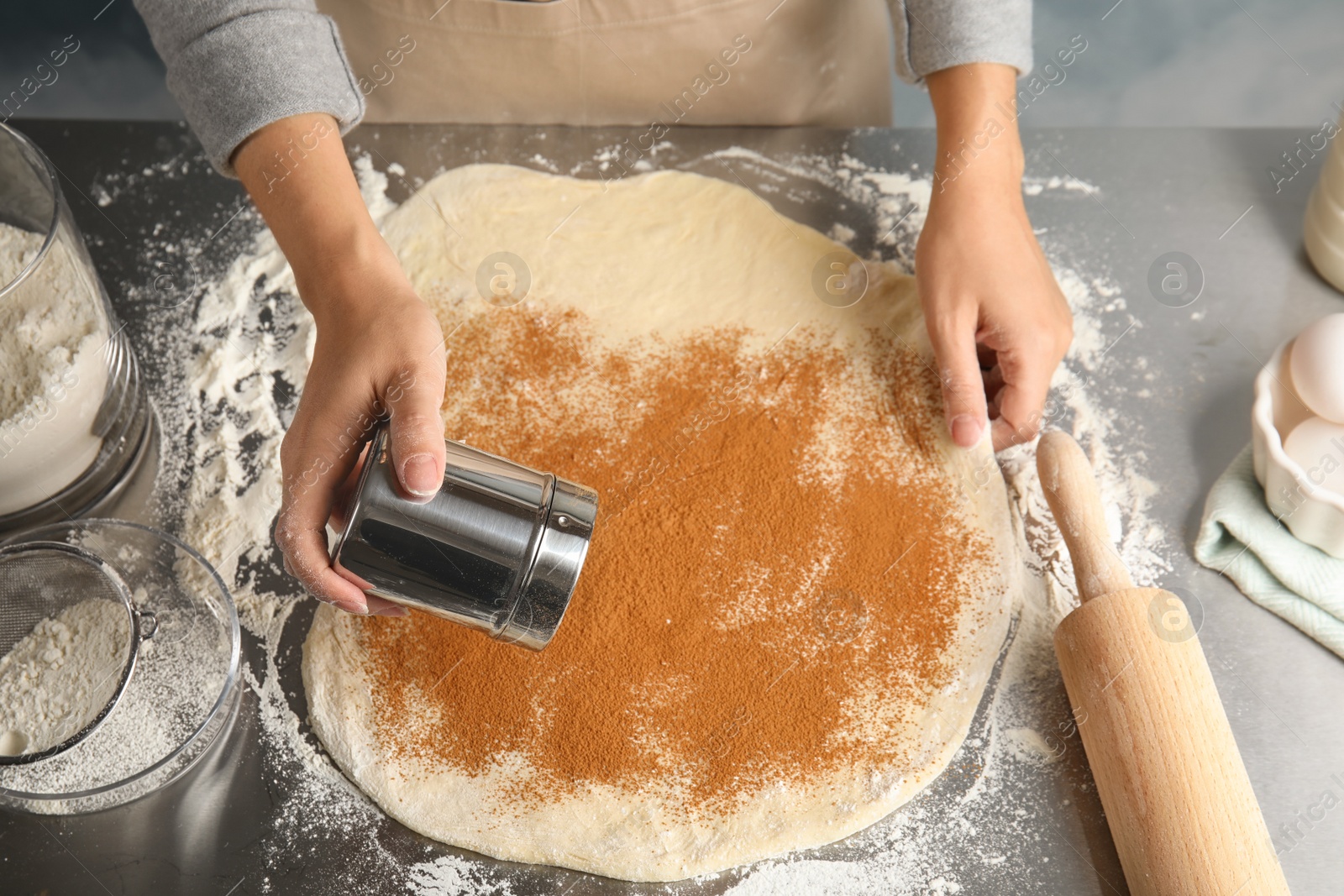 Photo of Woman making cinnamon rolls at table, closeup