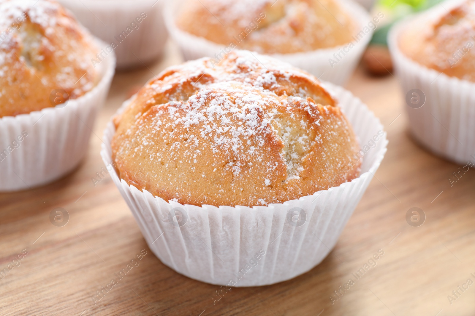 Photo of Tasty muffins powdered with sugar on wooden board, closeup